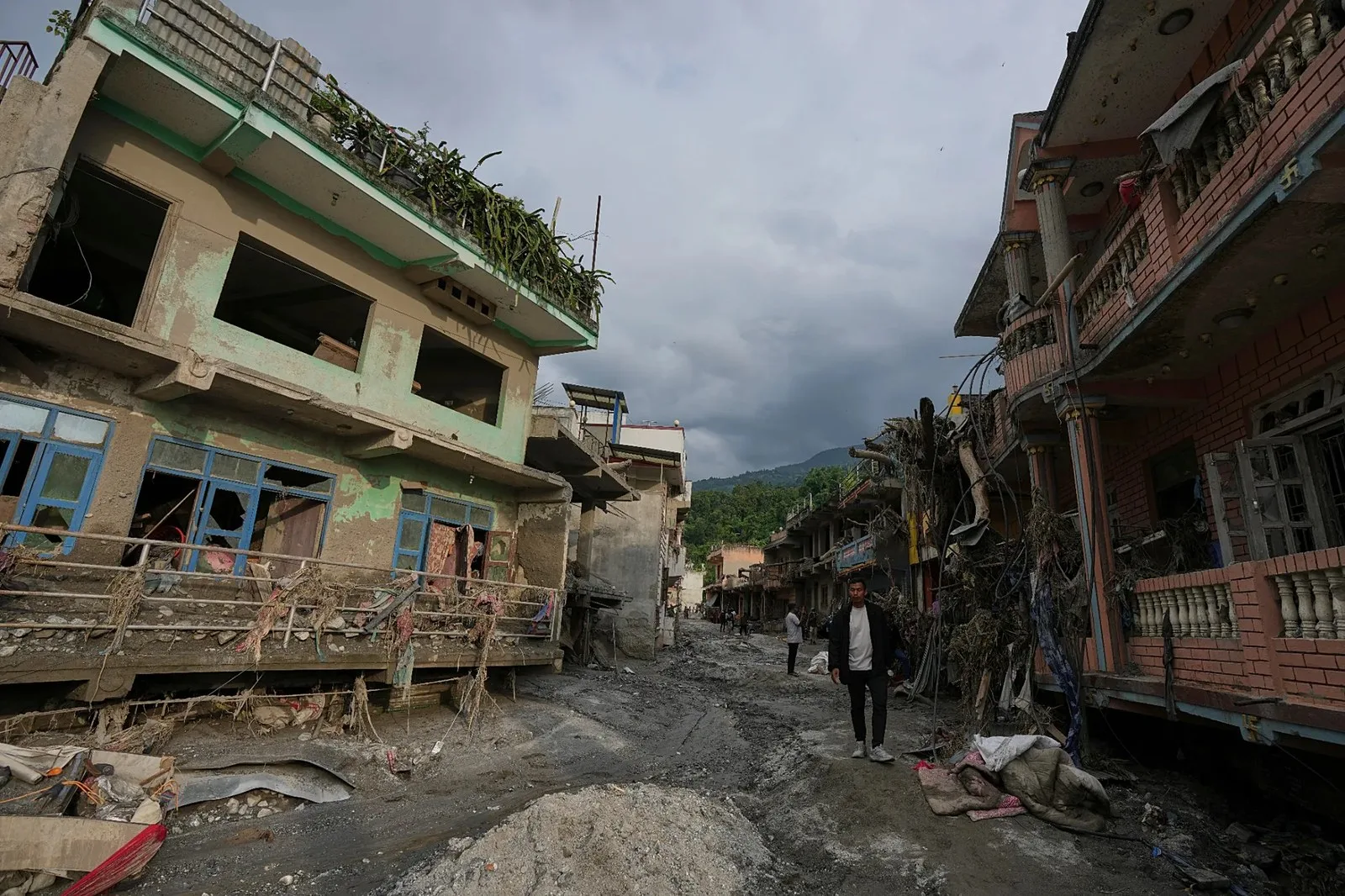Nepal'in Nuwakot bölgesindeki Devighat çevresinde ani selin ardından, hasar görmüş binaların sıralandığı bir caddede yürüyen insanlar, 28 Ağustos 2026