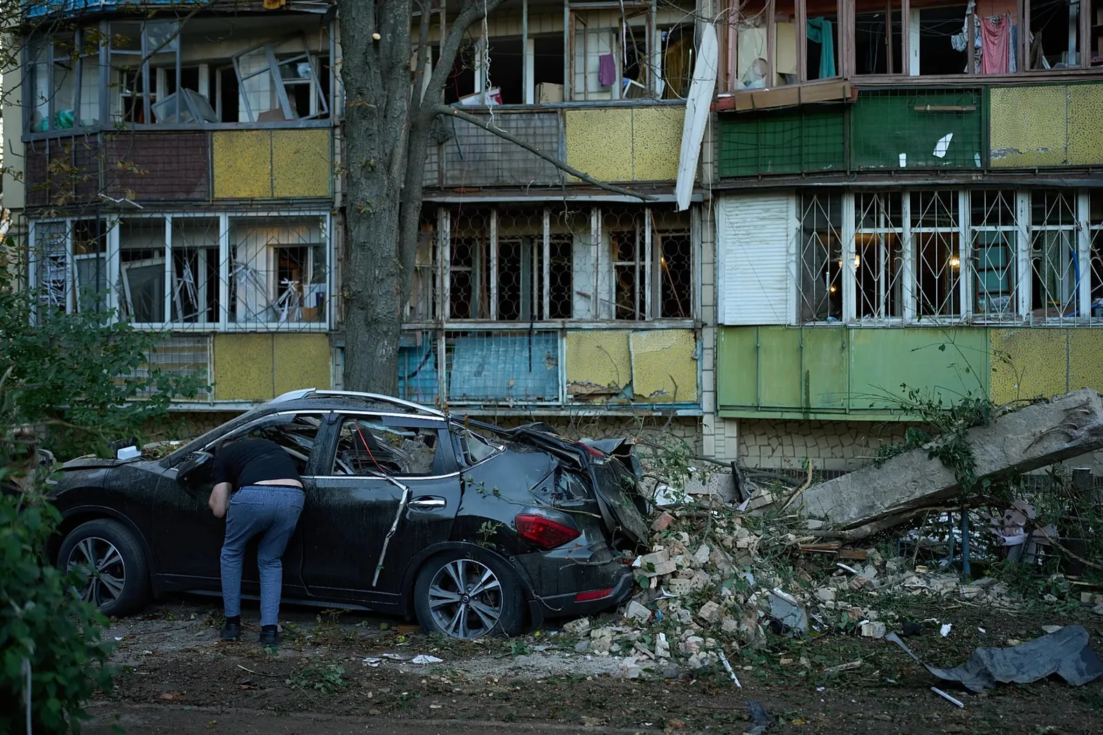 Kiev'de bir kişi, Rus saldırısının ardından ağır hasar gören konut binalarının yanında duran hurdaya dönmüş bir otomobilin içine bakıyor, 20 Ağustos 2026.