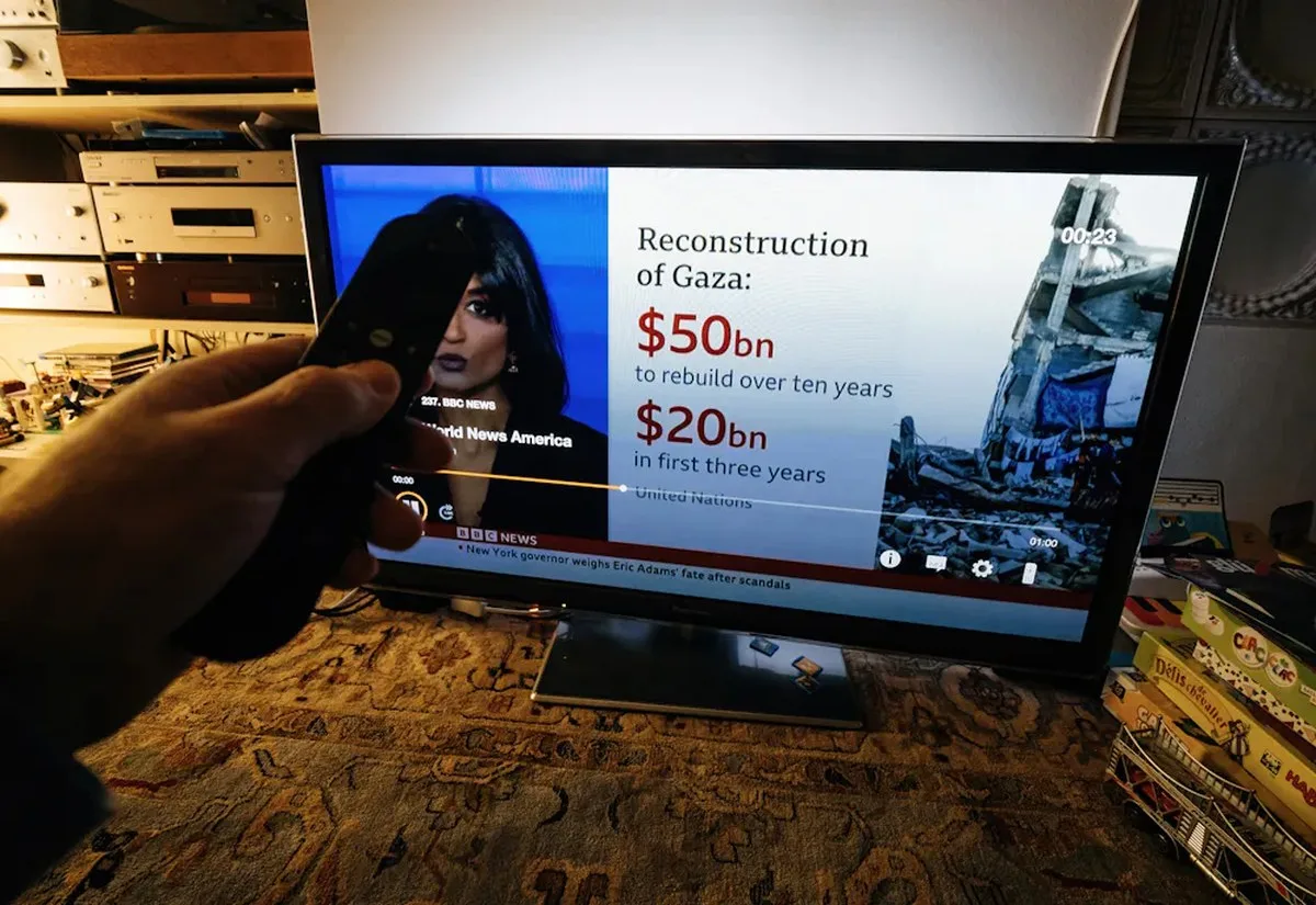 tv viewer pointing a remote control at a tv showing bbc news.