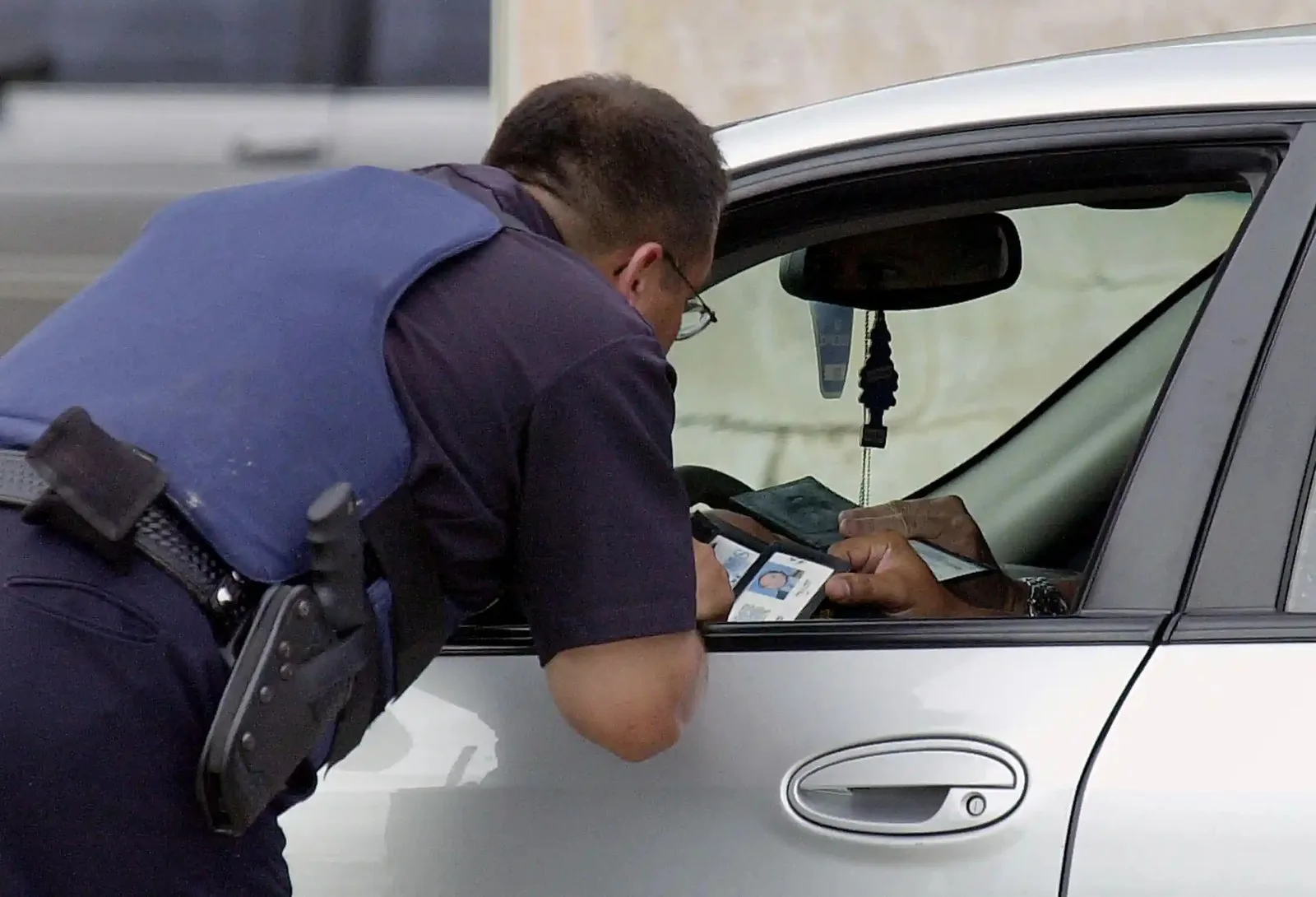 law enforcement officer leans into driver side of car looking at the ID the driver is holding out