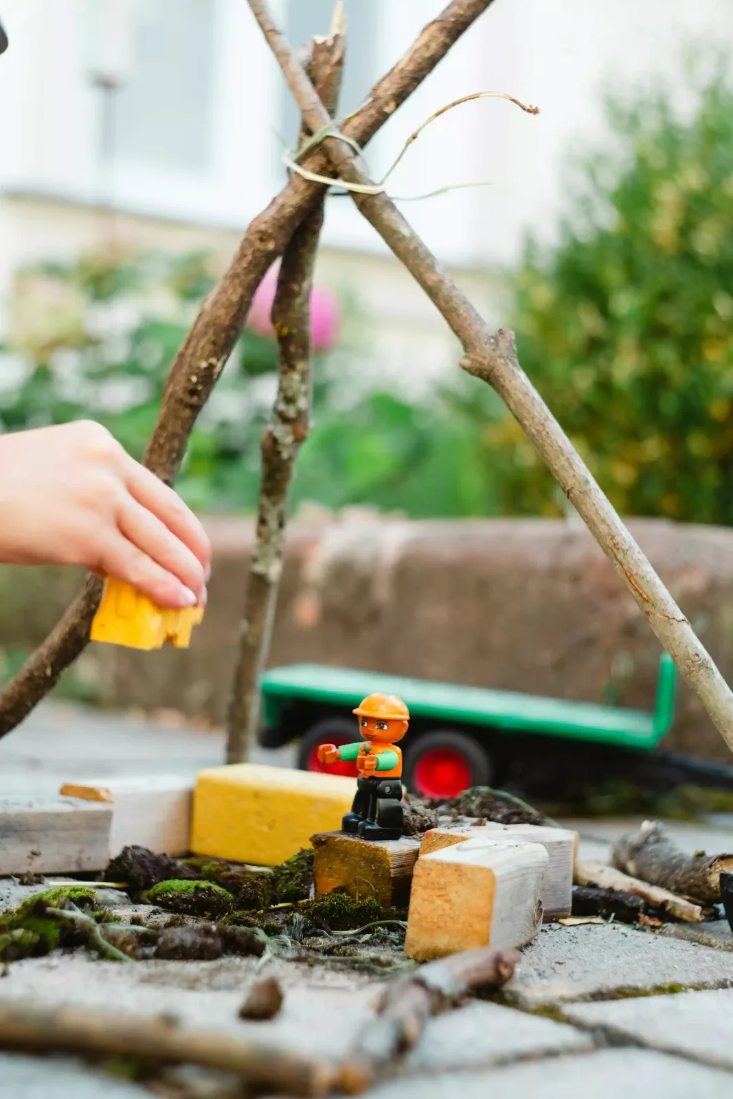 A child's hands playing with blocks and a stick structure outdoors.