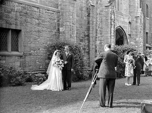 A newlywed couple standing in front of a church and their wedding photographer, Westmount, Montreal, 1945