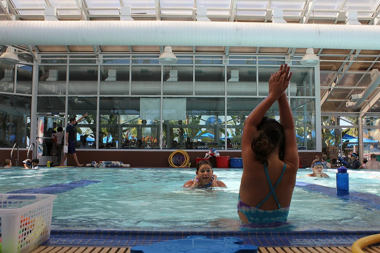 A five-year-old girl learns arm placement from her teacher in an individual class at a dedicated swimming school in San Jose, California. Other children learn in small group classes (far left and right).